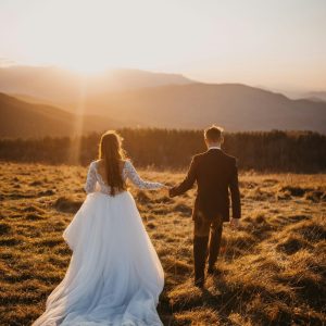 Man and woman in wedding dress walking on a grass field during daytime